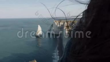 特写开心兴奋的旅游女用相机拍下Etretat岩石的照片，头发在风中缓慢地吹动。